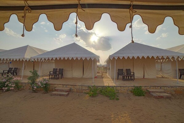 A desert camp with multiple tents, each with a covered seating area and a view of the desert landscape.