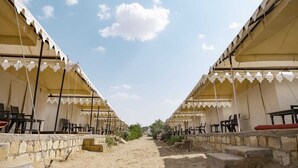 A row of tents with tables and chairs, a stone pathway, and a clear sky. - Royal Gadhvi Desert Camp (Jaisalmer)
