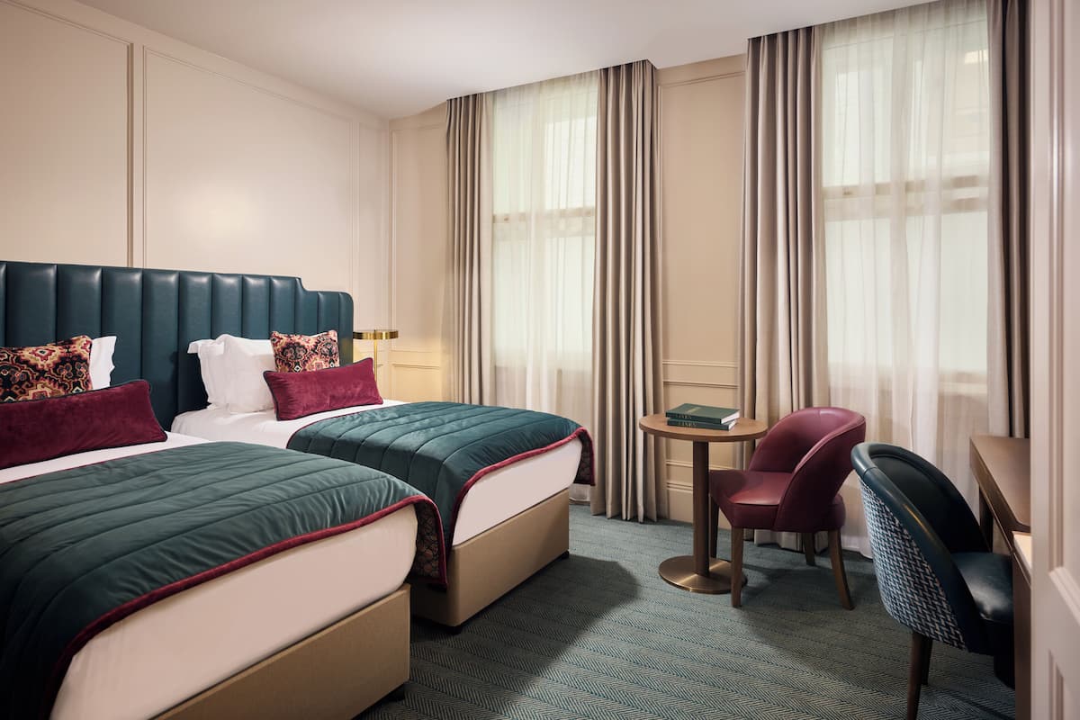 Une chambre d’hôtel avec deux lits, un bureau, une chaise et une vue sur l’extérieur grâce à de grandes fenêtres.