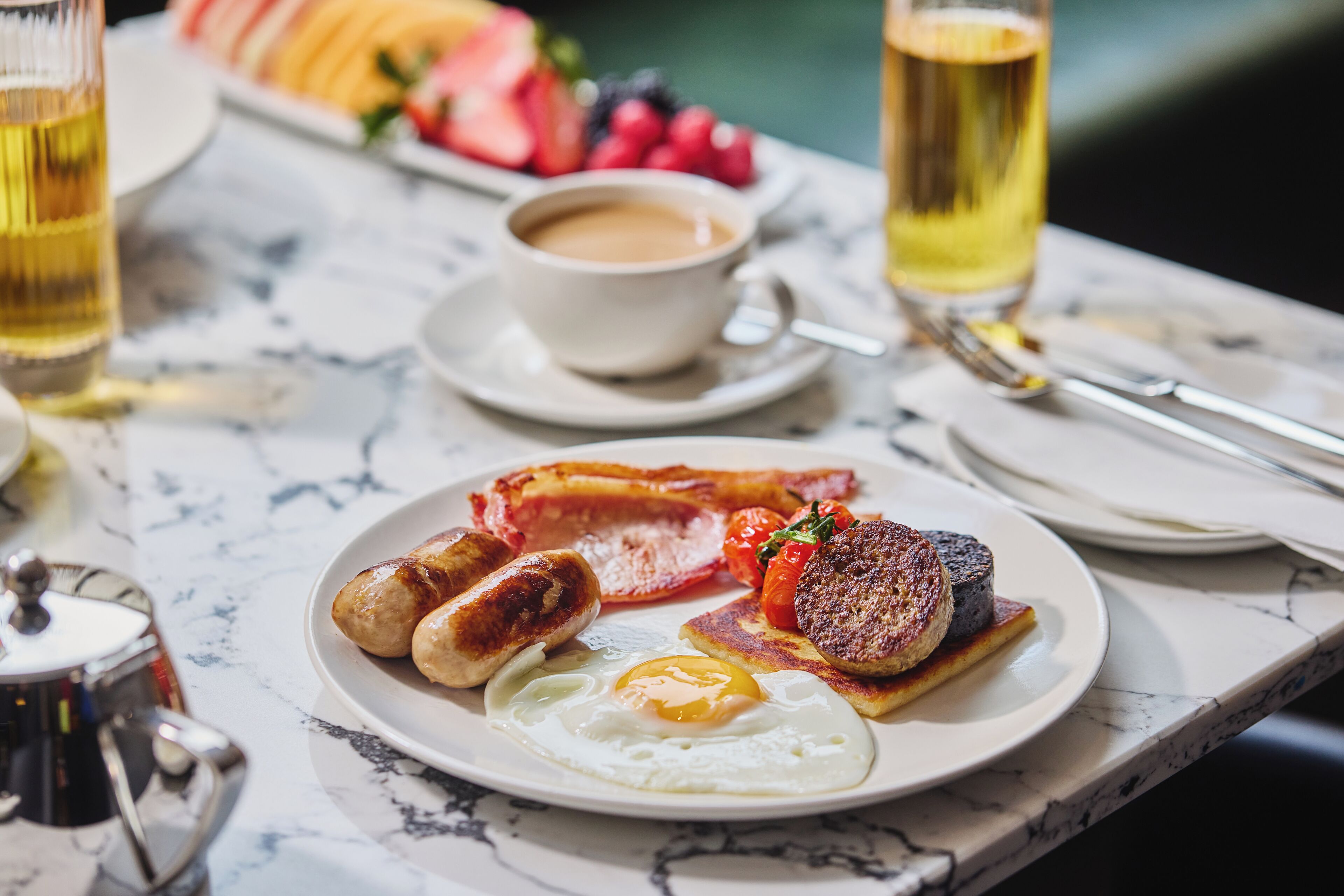 Un plato de desayuno con huevos, salchichas, tocino y tomates sobre una mesa de mármol.