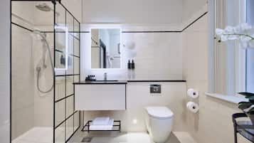 A modern bathroom with a glass shower enclosure, a toilet, a sink with a mirror, and a window with a plant.