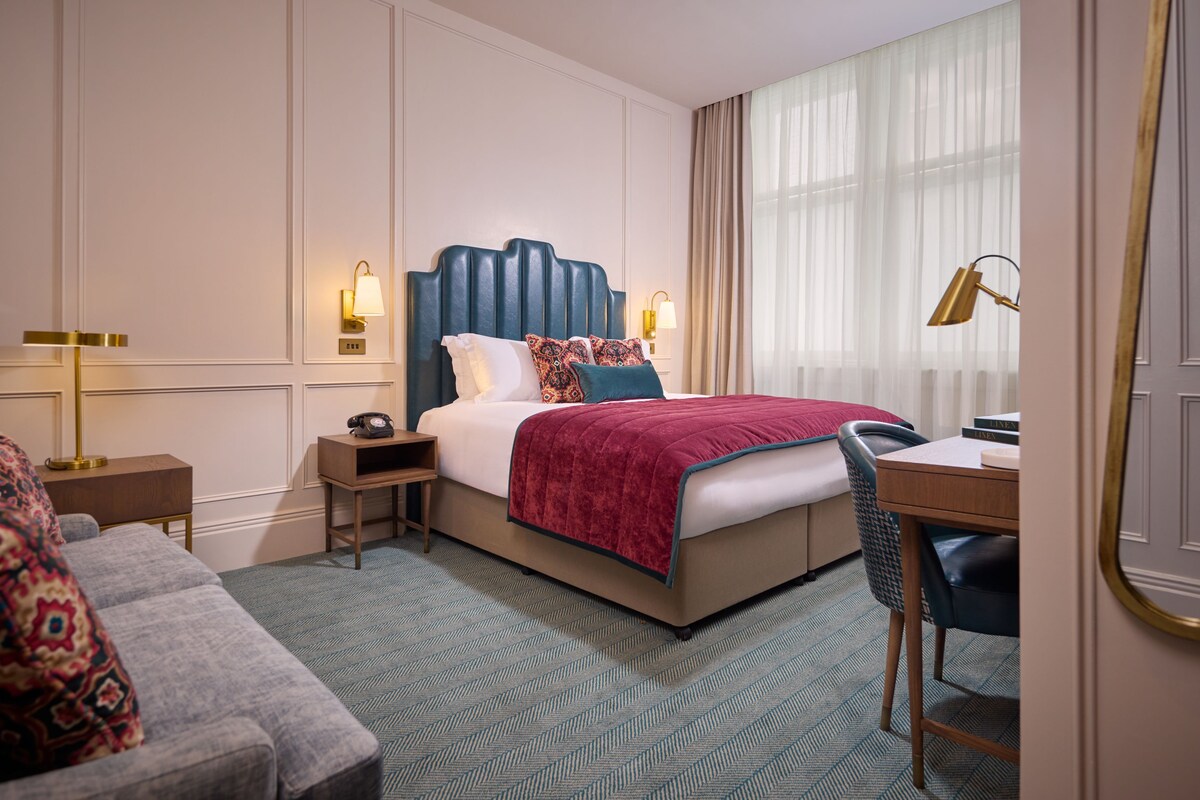 Une chambre d’hôtel comprenant un lit, un bureau, une chaise, une table de chevet et une lampe.