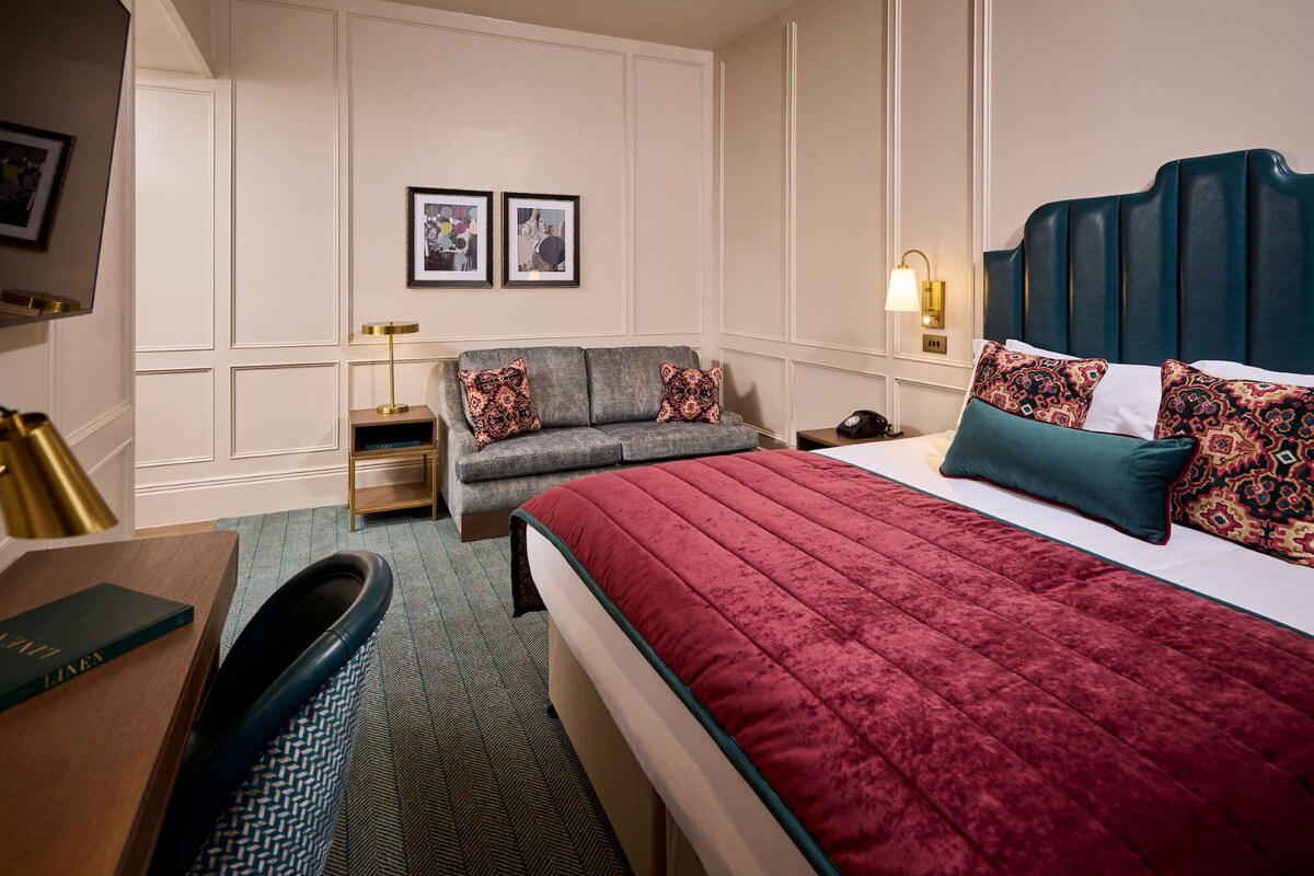 A hotel room with a bed, a desk, a chair, a sofa, and a nightstand.