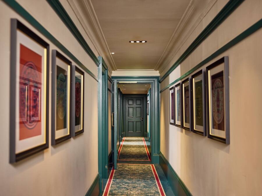 A hallway with framed artwork on the walls, a carpeted floor, and a door at the end.