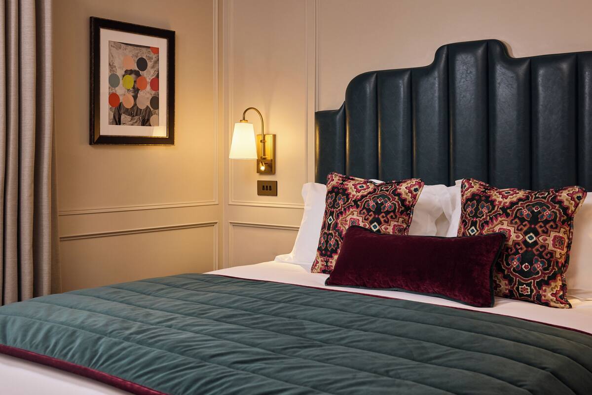 Une chambre d’hôtel avec un lit, une lampe fixée au mur et un tableau encadré.