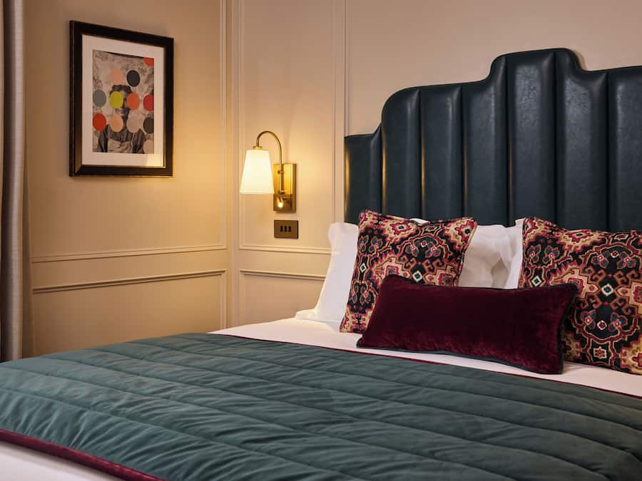 Una habitación de hotel con cama, una lámpara de pared y un cuadro enmarcado.