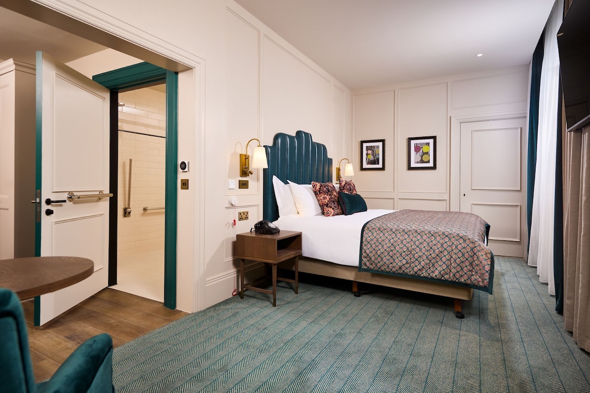 A hotel room with a bed, bedside table, and a chair.