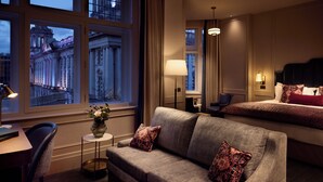 Une chambre d’hôtel avec une grande fenêtre, un canapé, un fauteuil, une table de chevet et une lampe.