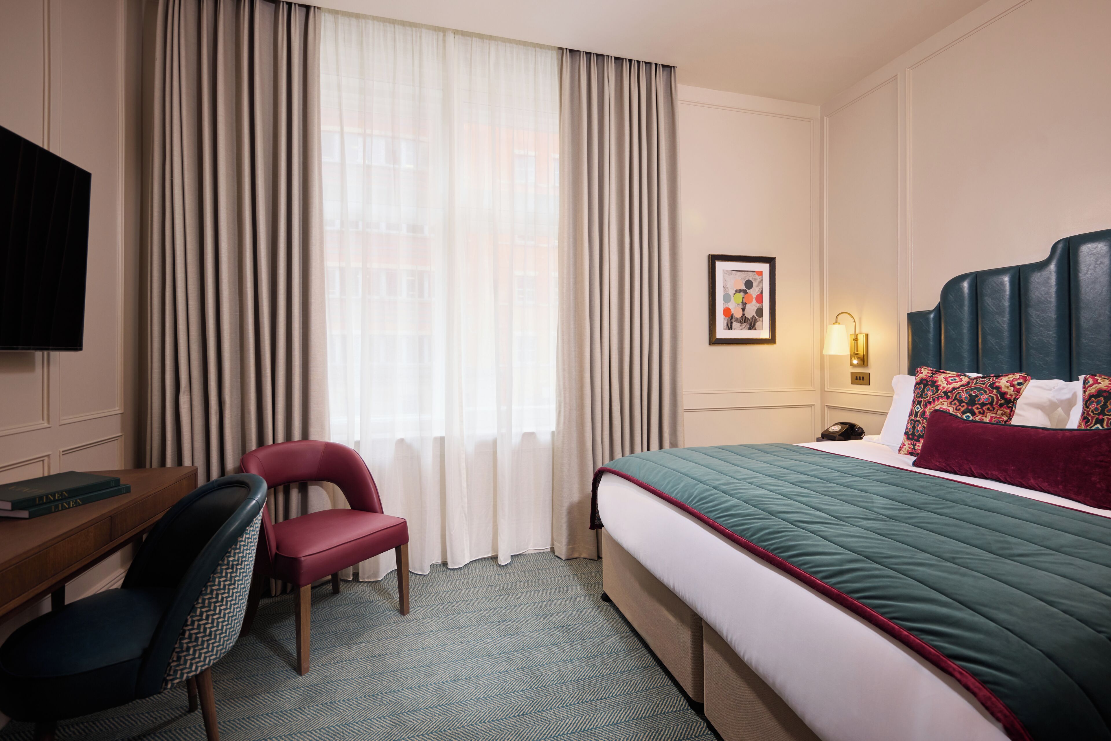 A hotel room with a bed, a desk, a chair, a television, and a window with curtains.