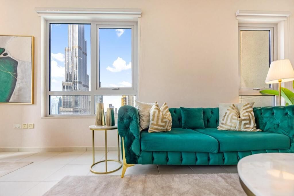 A teal sofa with gold and beige cushions, a gold side table, a round coffee table, and a view of a tall building through a window.