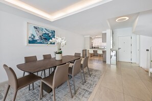 Un espace repas moderne avec une longue table, des chaises, une plante en pot et un grand tableau abstrait accroché au mur.