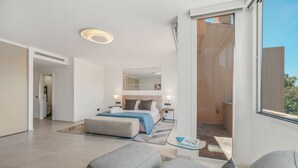 Ein modernes Hotelzimmer mit einem großen Bett, einer Sitzecke mit Sofa, einem kleinen Tisch und einem Balkon mit Aussicht.