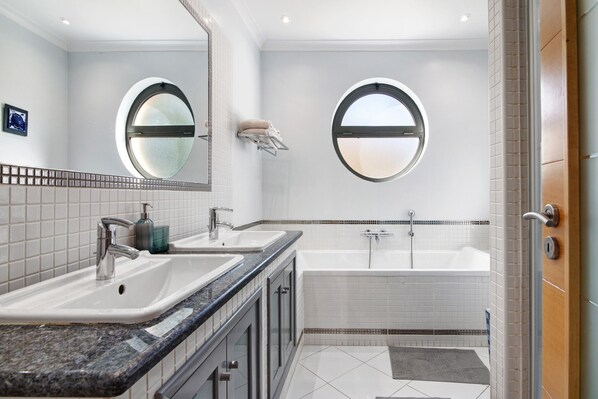 A modern bathroom with two sinks, a bathtub, and two round windows.