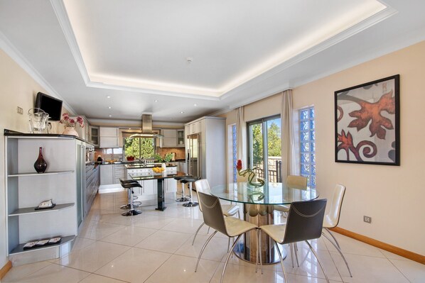 Una cocina moderna con comedor, un televisor en un estante y un amplio ventanal.