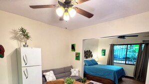 A compact living space with a dining table, chairs, a sofa, a bed, a ceiling fan, and a refrigerator. - Tiny Paradise Ground Floor Studio (Playas Del Coco)