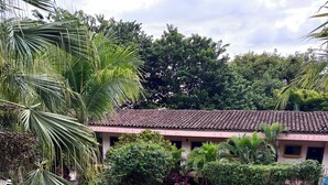 A swimming pool surrounded by lush greenery and a building with a tiled roof. - Tiny Paradise Ground Floor Studio (Playas Del Coco)