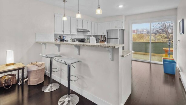 A modern kitchen with white cabinets, stainless steel appliances, and a bar area with stools. - Quidi Vidi King 3 Doubles Parking Office (St. John's)