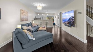A modern living room with a grey sofa, a flat-screen TV, and a chandelier. - Quidi Vidi King 3 Doubles Parking Office (St. John's)
