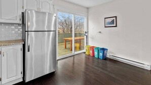 A kitchen with a stainless steel refrigerator, white cabinets, and a sliding glass door leading to an outdoor patio. - Quidi Vidi King 3 Doubles Parking Office (St. John's)