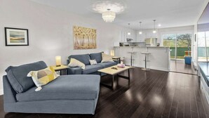 A modern living room with a grey sofa, a coffee table, and a chandelier. - Quidi Vidi King 3 Doubles Parking Office (St. John's)