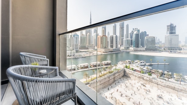 Un balcone con due sedie in vimini, ringhiera in vetro e vista sullo skyline cittadino e sul lungomare.