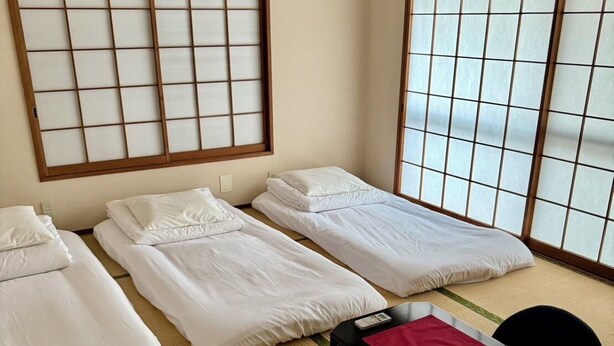 A room with three single beds, a tatami mat floor, a small table with a red placemat, and a black chair. - Camellia House, Tokyo, Zoshigaya, walkable to Ikebukuro station & Sunshine City (豊島区雑司が谷)