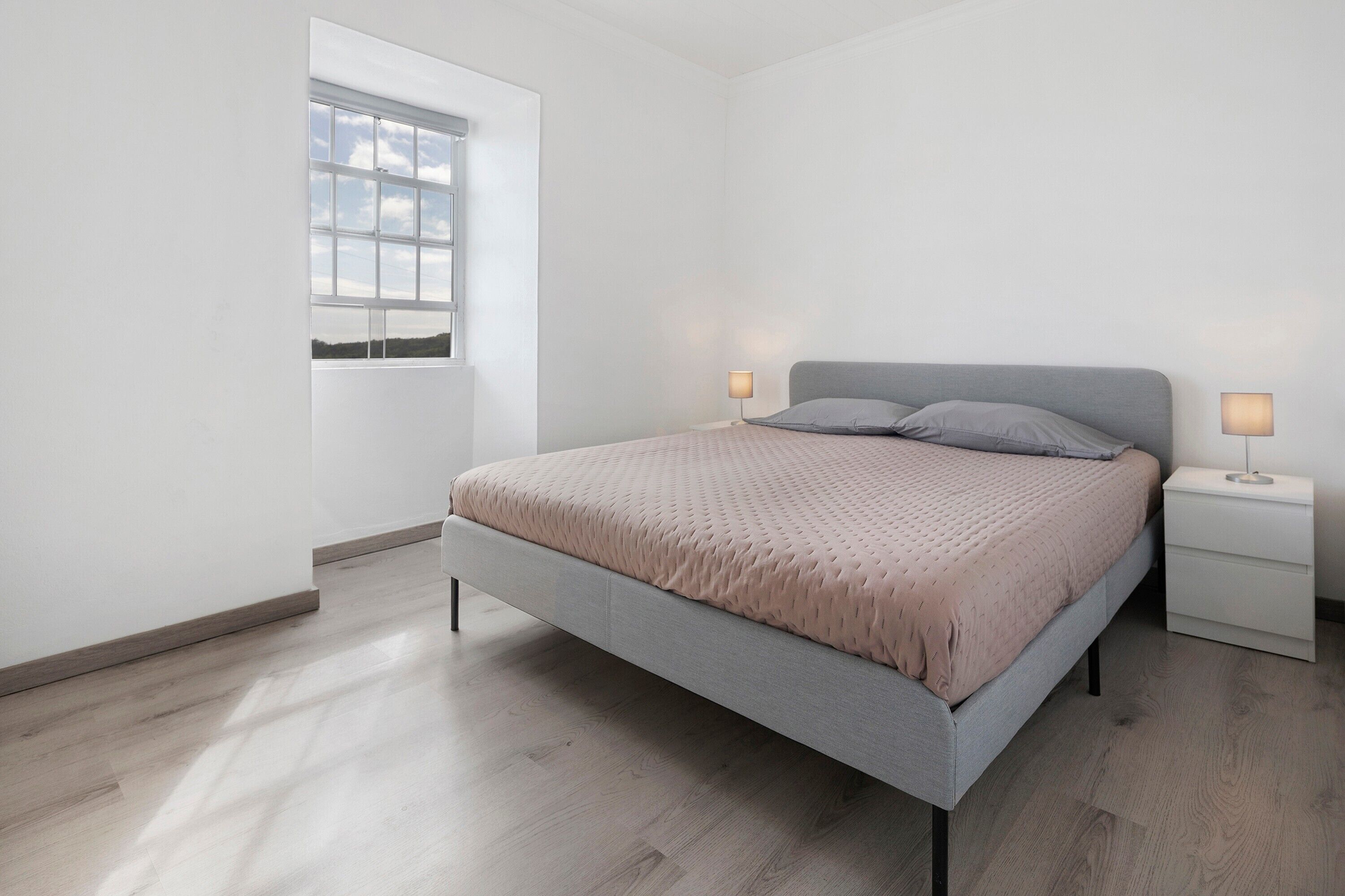 Un dormitorio moderno con cama, mesitas de noche y ventana.