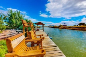 A wooden dock with benches extending over a calm body of water, surrounded by greenery and a clear sky. - Break Point Cottage | Canal-Front Stay w/ Pool Table Fun (Rockport)