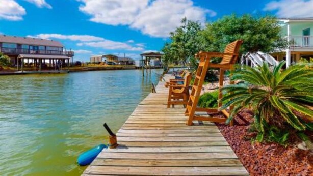 A wooden dock extending into calm water, with lounge chairs and a small structure on the right. - Break Point Cottage | Canal-Front Stay w/ Pool Table Fun (Rockport)