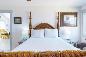 A bedroom with a four-poster bed, a framed picture on the wall, and a small table with a lamp. - Break Point Cottage | Canal-Front Stay w/ Pool Table Fun (Rockport)