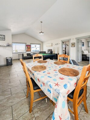 A dining area with a pool table, wooden chairs, and a tablecloth with a sea theme. - Break Point Cottage | Canal-Front Stay w/ Pool Table Fun (Rockport)
