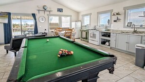 A pool table with balls, a dining area with chairs, a kitchen with appliances, and a clock on the wall. - Break Point Cottage | Canal-Front Stay w/ Pool Table Fun (Rockport)