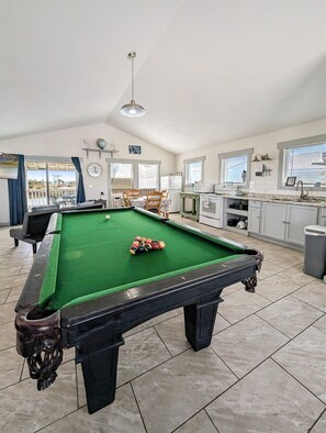 A pool table with balls, a dining area with chairs, a kitchen with appliances, and a clock on the wall. - Break Point Cottage | Canal-Front Stay w/ Pool Table Fun (Rockport)
