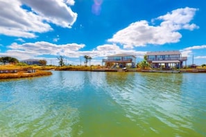 A waterfront property with two modern houses, a calm lake, and a clear sky. - Break Point Cottage | Canal-Front Stay w/ Pool Table Fun (Rockport)