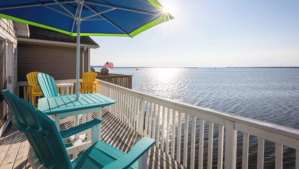 A deck with chairs and a table, overlooking a calm body of water. - New Listing! Water Views, Sunsets and Much More! (Kill Devil Hills)