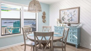 A dining area with a view of the water, a woven light fixture, a blue dresser, and a framed artwork. - New Listing! Water Views, Sunsets and Much More! (Kill Devil Hills)