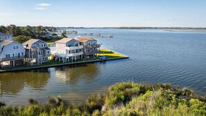 A waterfront property with multiple houses, a dock, and a grassy shoreline. - New Listing! Water Views, Sunsets and Much More! (Kill Devil Hills)