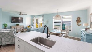 A kitchen with a sink, a dining area with chairs, a ceiling fan, and a view of the sea through large windows. - New Listing! Water Views, Sunsets and Much More! (Kill Devil Hills)