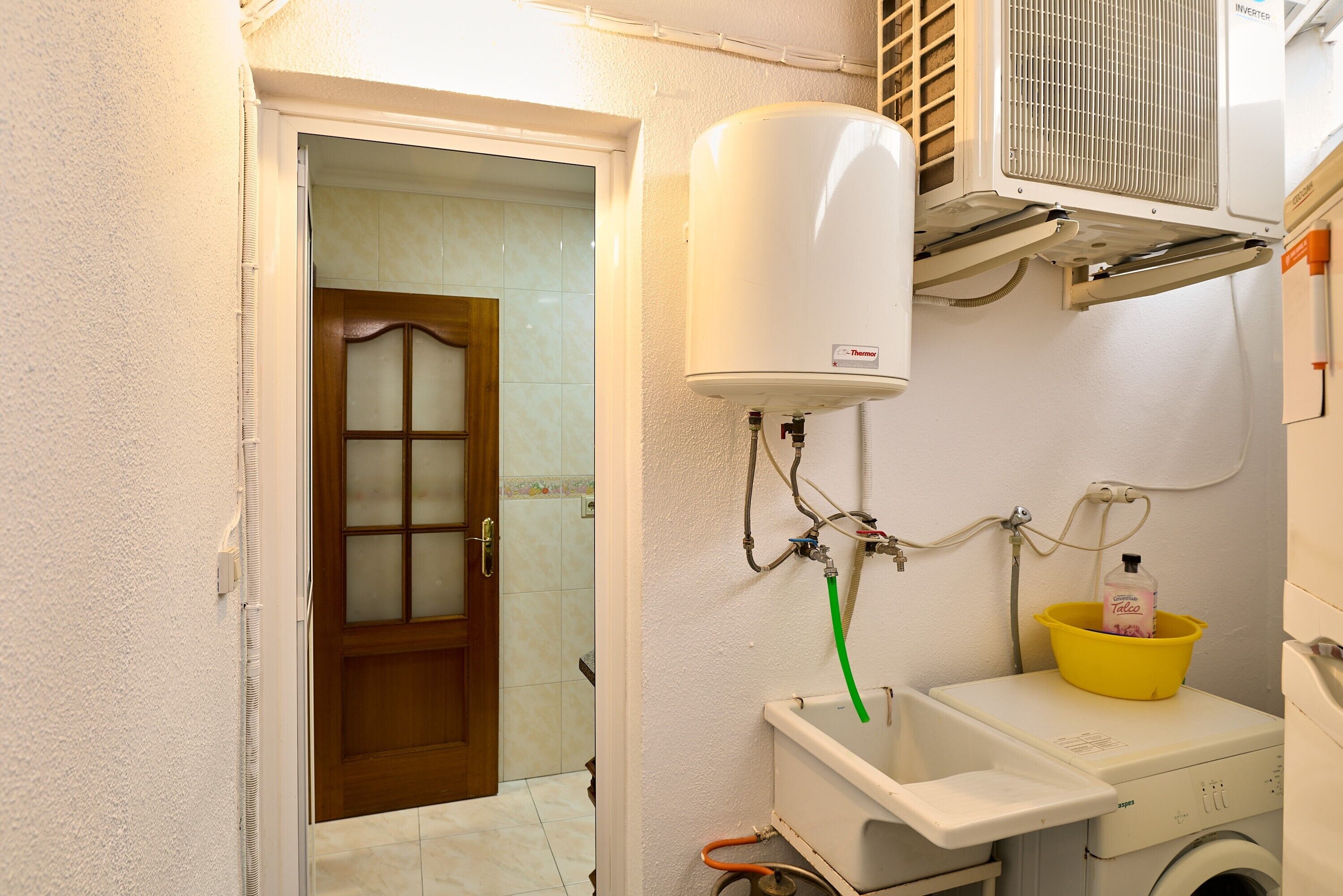 Un baño con un calentador blanco, un lavabo amarillo y una lavadora.
