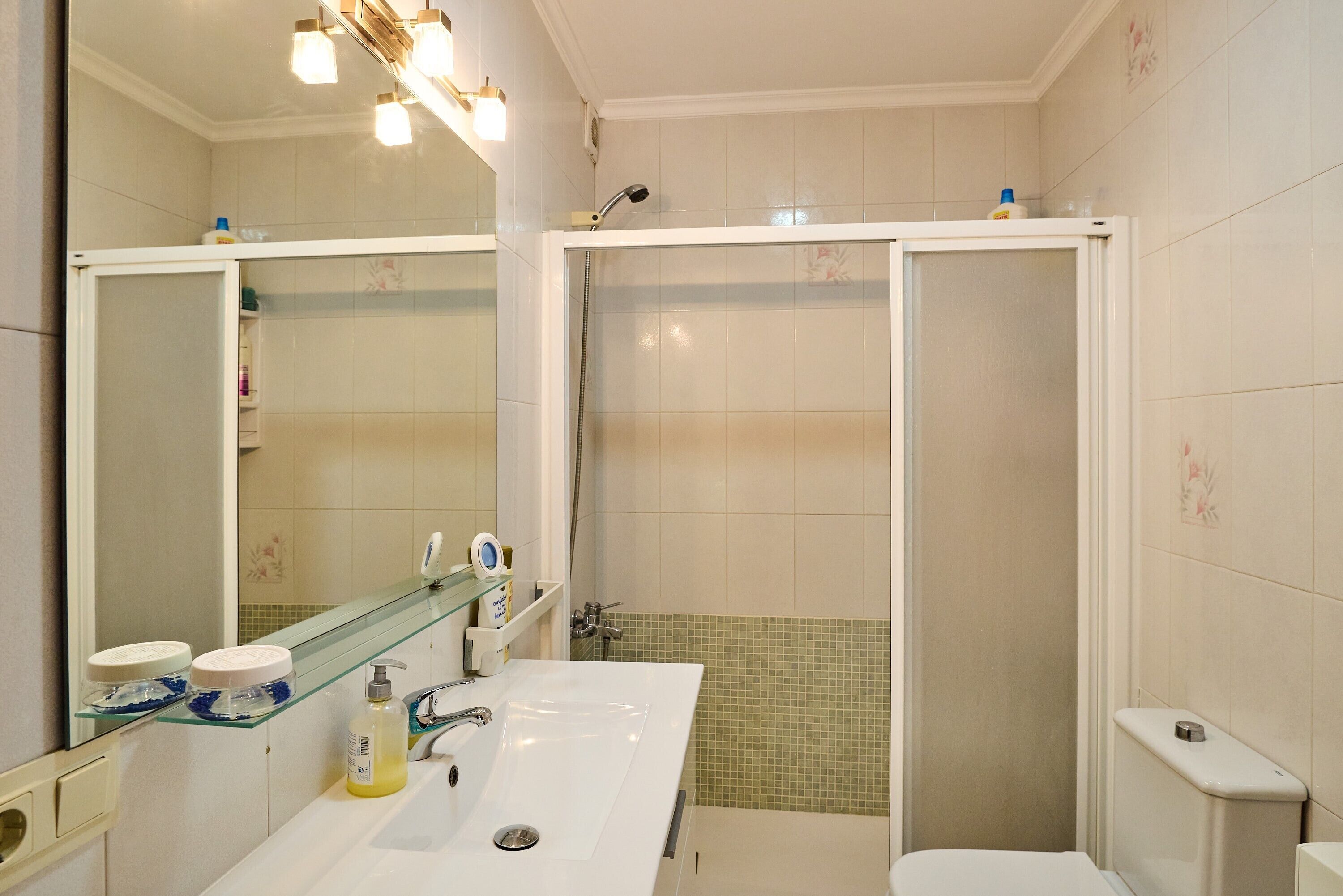 Een badkamer met een wit wastafelmeubel, een glazen plank, een spiegel, een douchecabine en een toilet.