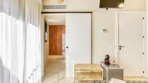Een hotelkamer met een bed, een klein tafeltje met een waterkoker, een televisie en een deur naar een badkamer.