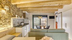 Een modern interieur met een stenen muur, houten balken in het plafond, een kitchenette, een zithoek met een bank en een tafel, en een schuifdeur naar buiten.