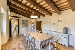 Un coin repas avec une table dressée pour six personnes, des poutres en bois au plafond et un luminaire suspendu au-dessus.