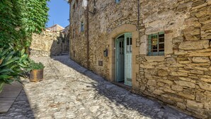 Una stretta via acciottolata con edifici in pietra, una panchina di legno e un cartello che indica un luogo.