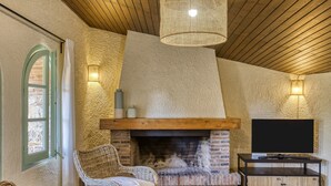 Una camera accogliente con camino, televisore su un supporto in legno, poltrone in vimini e un lampadario.