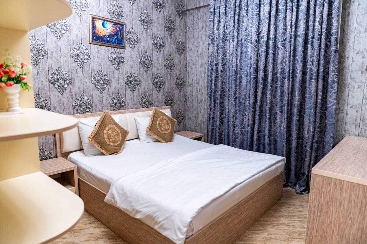 A neatly arranged bedroom with a bed, bedside tables, a lamp, and a painting on the wall.