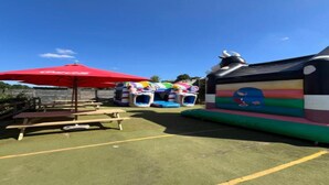 An outdoor area with inflatable bounce houses, picnic tables, and a red umbrella. - Camping Tent With Modern Amenities (Trois-Ponts)