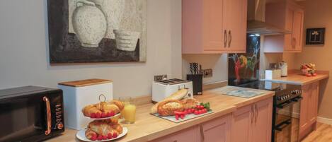 Une cuisine moderne avec des meubles roses, un four à micro-ondes, un grille-pain et un verre de jus d’orange posé sur le comptoir.