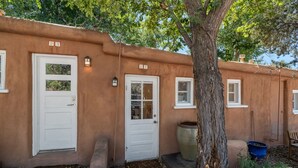 A stucco building with two white doors and windows, a large tree, and a blue planter. - New Listing! Charming Adobe Escape | Walk to Canyon Road & Galleries (Santa Fe)