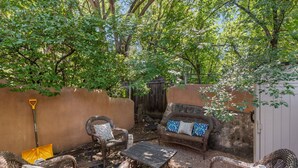 An outdoor patio with wicker furniture, a coffee table, and a broom leaning against a wall. - New Listing! Charming Adobe Escape | Walk to Canyon Road & Galleries (Santa Fe)